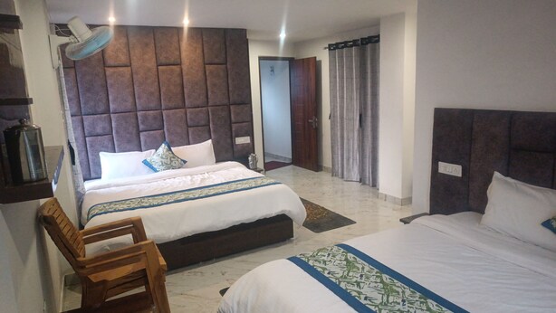 Habitación de hotel con dos camas, una silla de madera, un ventilador y un cabecero grande y acolchado.