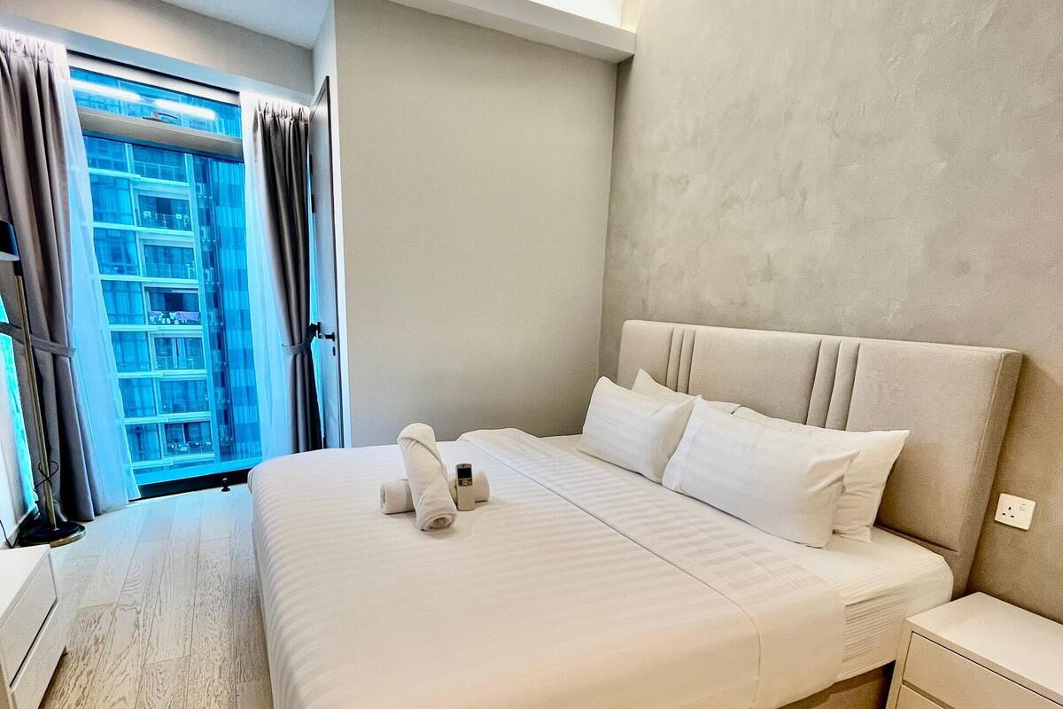 A modern hotel room with a large bed, a ceiling fan, a nightstand, and a view of a building through the window.