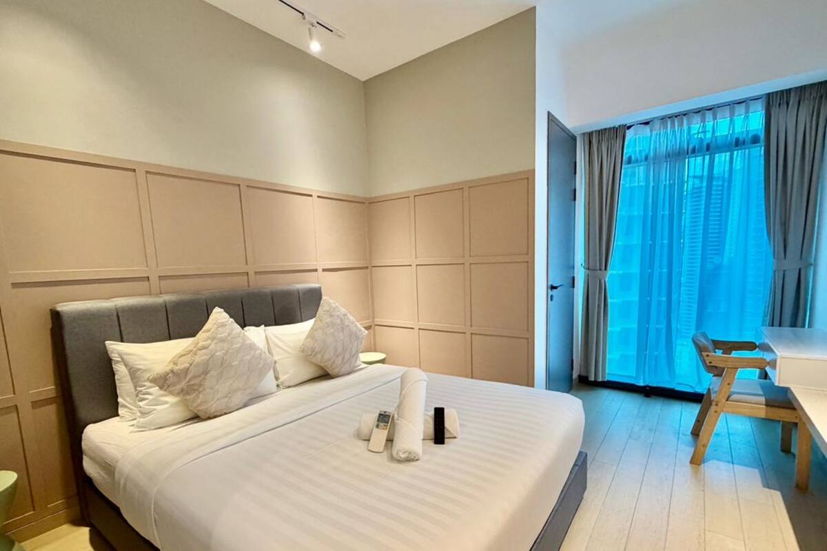 A hotel room with a large bed, a bedside table, a chair, and a window with curtains.