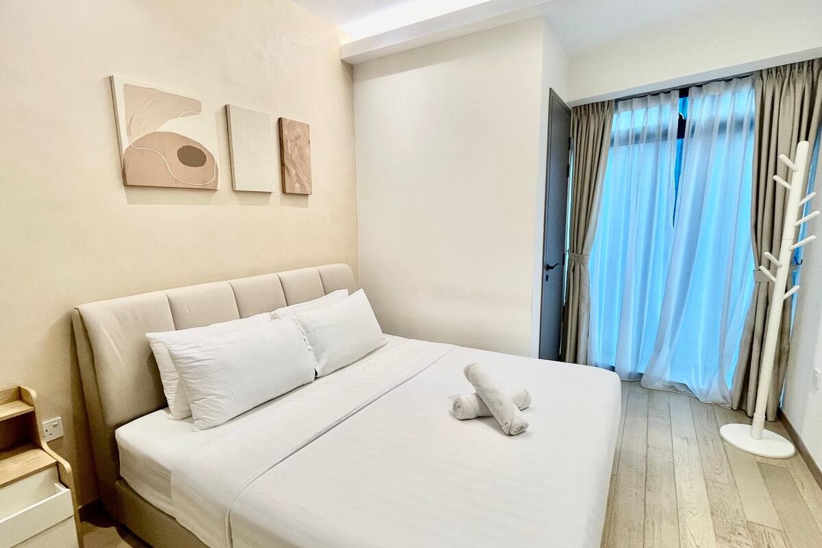 A hotel room with a large bed, a bedside table, a wardrobe, and a window with curtains.