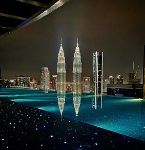 A nighttime cityscape with illuminated skyscrapers and a reflective pool. - Eaton Residences by ubook (Kuala Lumpur)