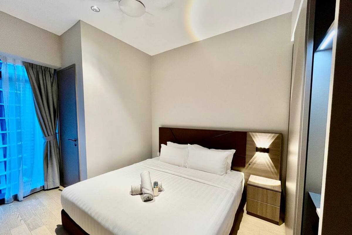 A hotel room with a neatly made bed, a bedside table with a lamp, and a door leading to a balcony.