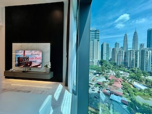 Een modern interieur met een tv waarop 'Morning Cafe Music' draait, een stadsgezicht en een raam met uitzicht op een parkeerplaats.