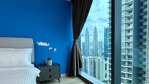 A bedroom with a bed, a nightstand, a potted orchid, and a large window with a cityscape view. - Eaton Residences by ubook (Kuala Lumpur)