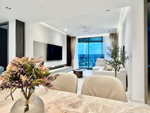 Een moderne woonkamer met een flatscreen televisie, een eettafel met een bloemenvaas, een bank en uitzicht op de stad.