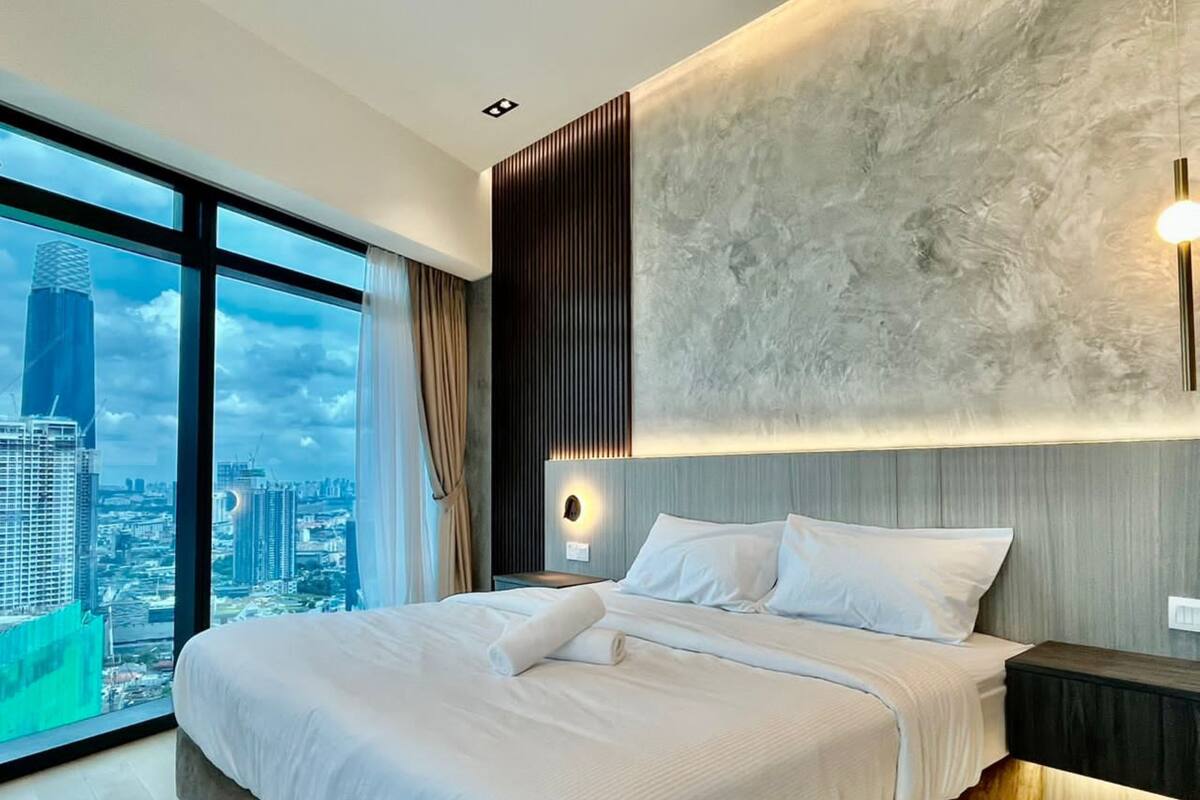 A modern hotel room with a large bed, a city view, and a unique textured wall.