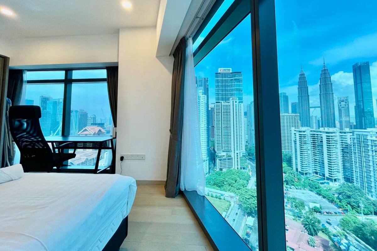 A hotel room with a bed, a desk, and a large window offering a cityscape view.