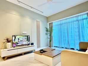A modern living room with a flat-screen TV, a coffee table, a sofa, and a large window with sheer curtains. - Eaton Residences by ubook (Kuala Lumpur)