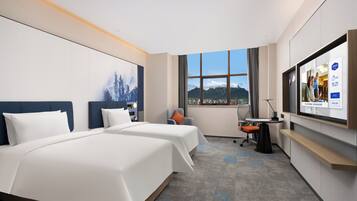 A hotel room with two beds, a desk, a chair, a TV, and a window with a mountain view.
