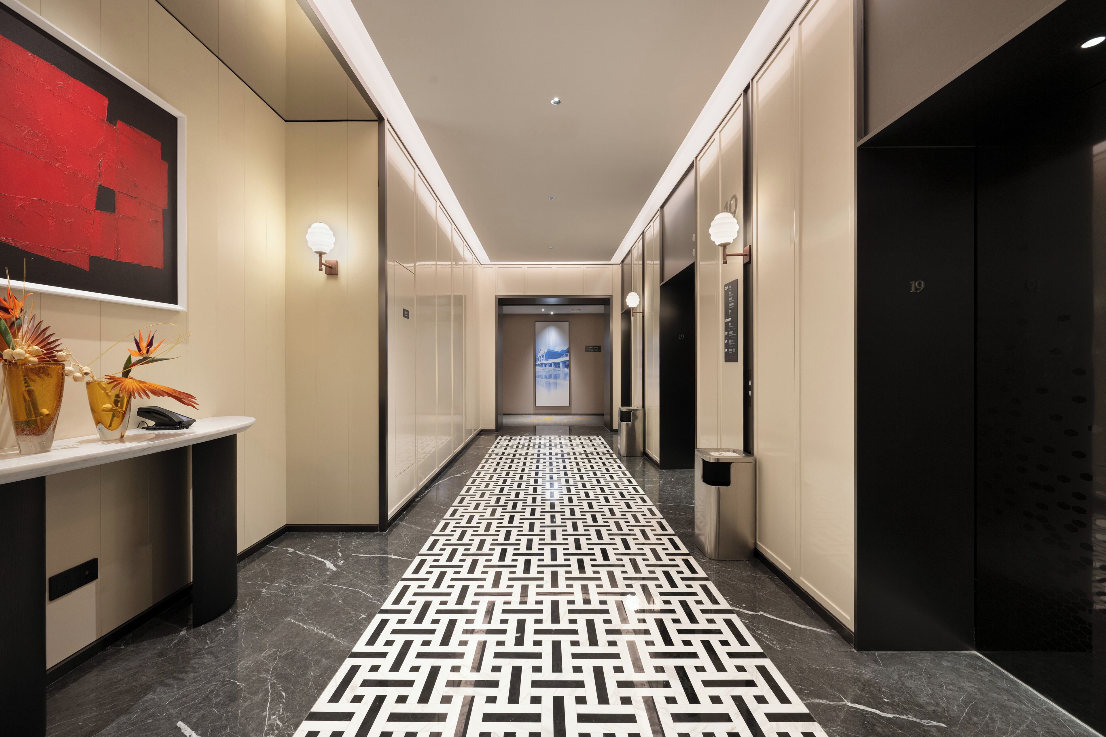 Ein moderner Hotelgang mit einem geometrisch gemusterten Boden, einer Rezeption und Aufzugtüren.