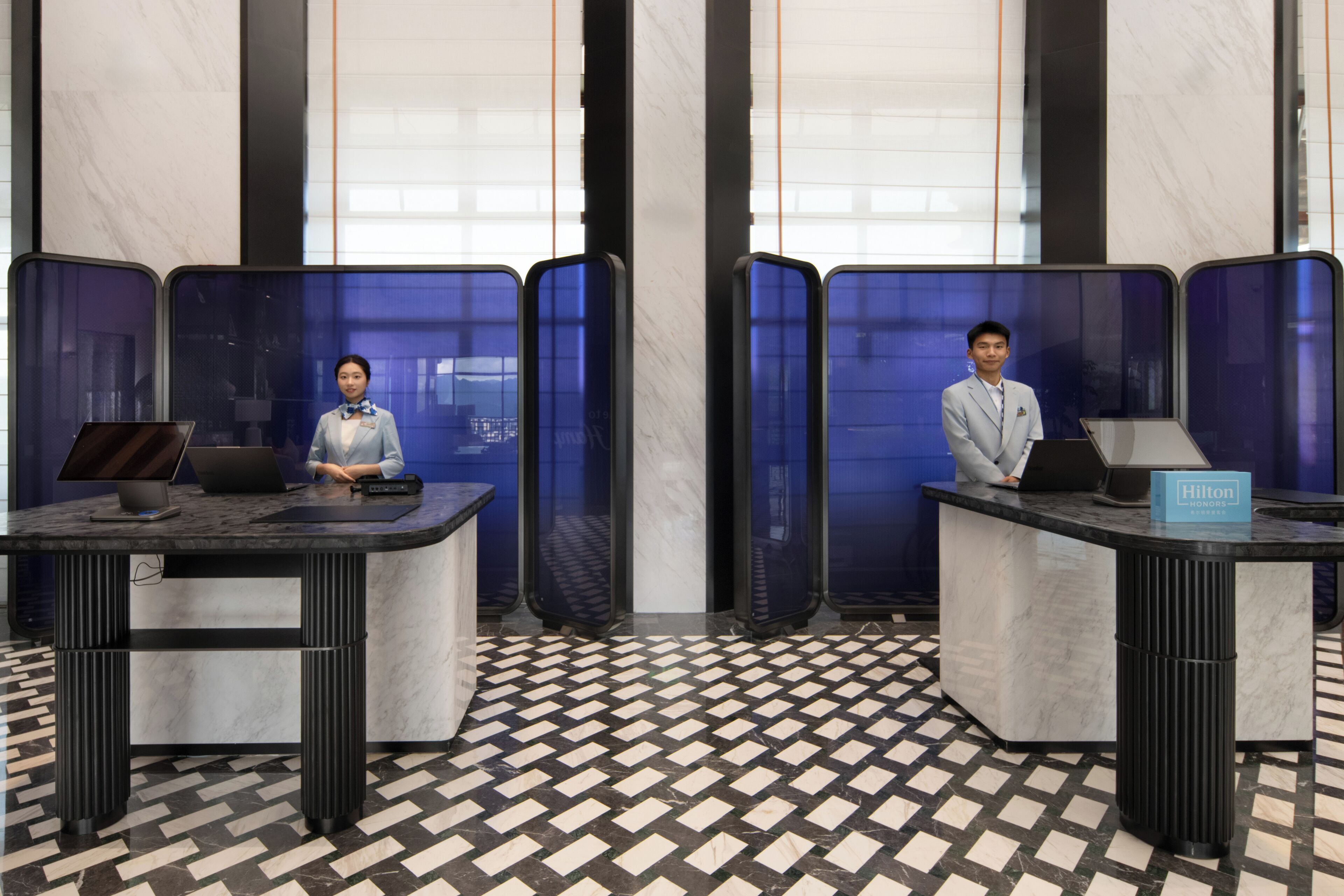 A hotel reception desk with a check-in counter, a computer, and a sign indicating the hotel name.