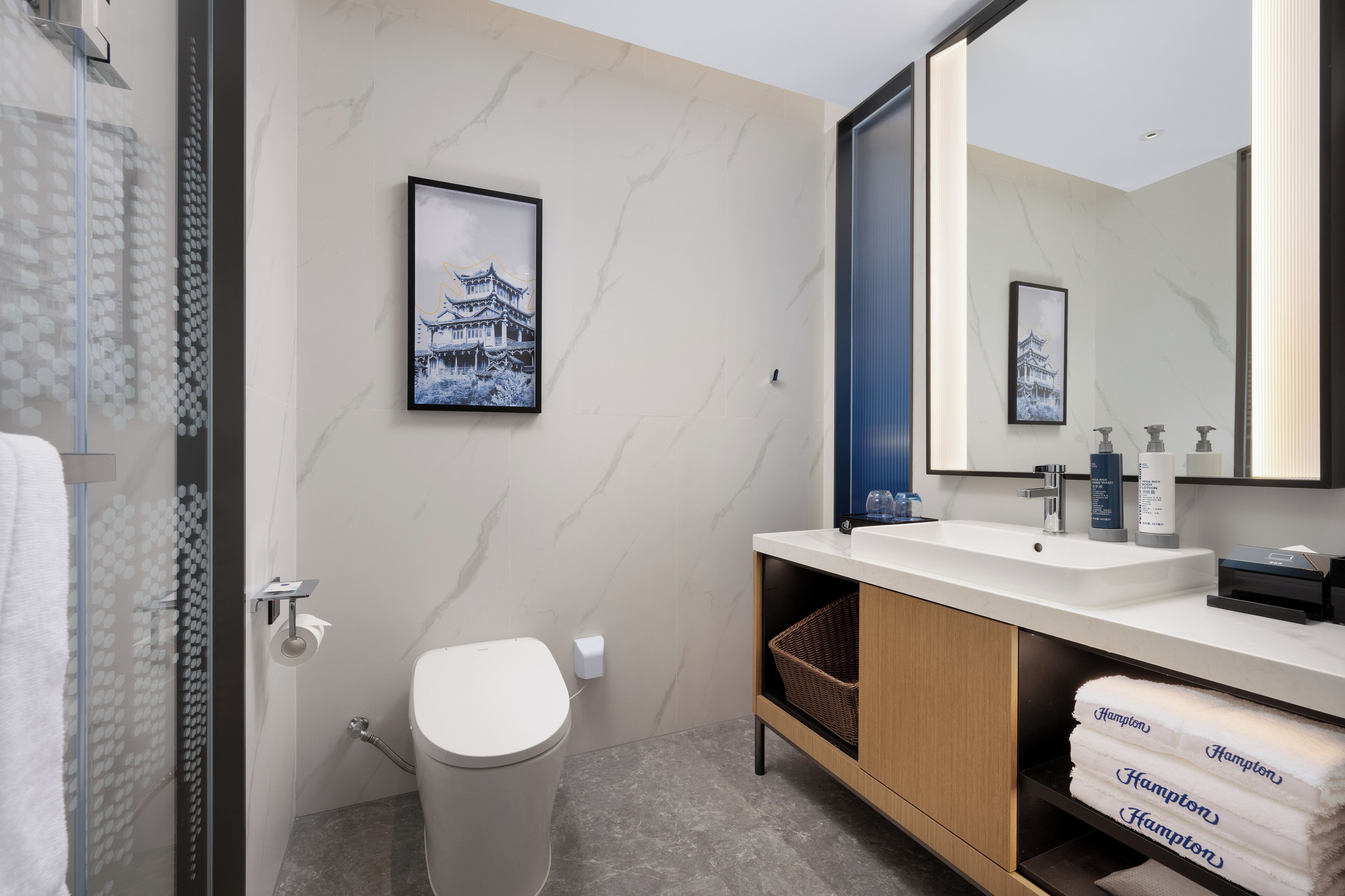 Un baño moderno con inodoro, lavamanos y ducha. Hay toallas y una cesta en la encimera.
