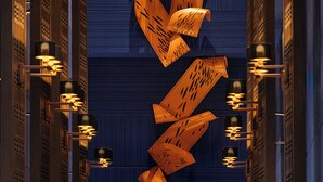 Un pasillo con pared azul, una gran escultura de madera y una silla blanca.