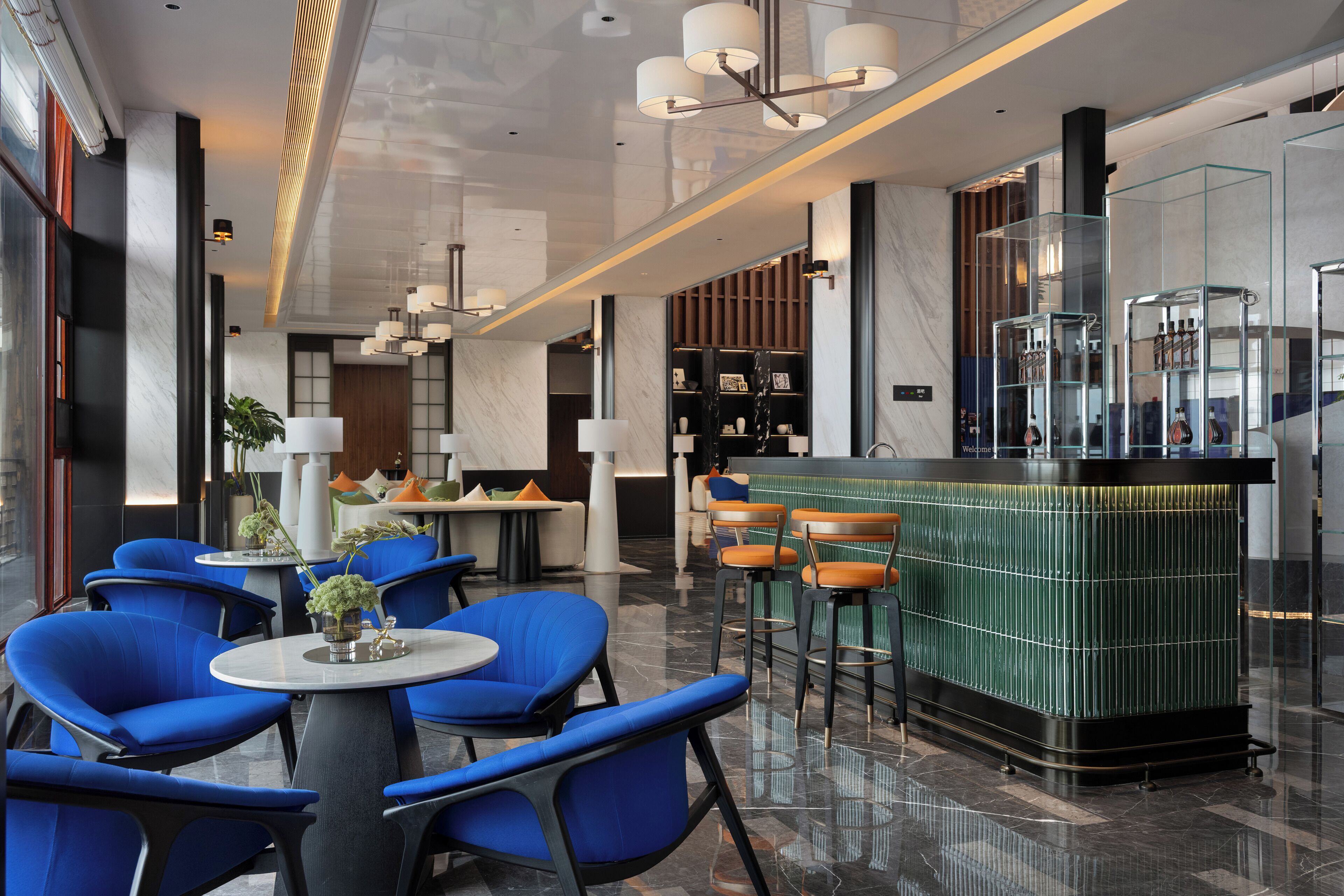 Eine moderne Hotelhalle mit blauen Stühlen, einer zentralen Bar und einem polierten Marmorboden.