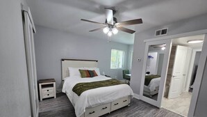 Ein Schlafzimmer mit Bett, Nachttischen, Deckenventilator und Spiegel.