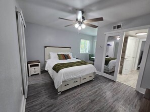 A bedroom with a bed, bedside tables, a ceiling fan, and a mirror.