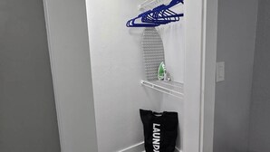 Ein Waschraum mit weißer Wand, einem blauen Wäscheständer, einer grünen Flasche und einem schwarzen Wäschebeutel.