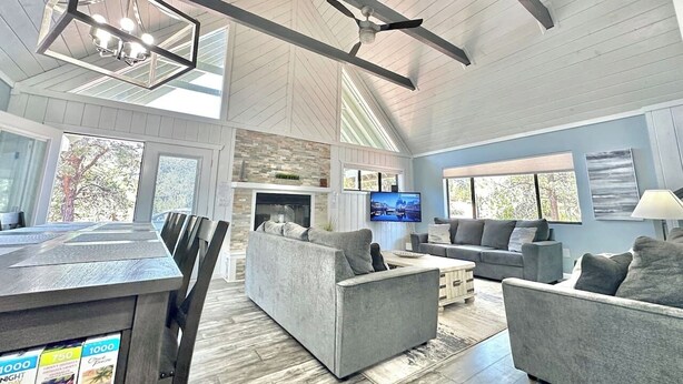 A spacious living room with a fireplace, grey sofas, a TV, and a dining area with a wooden table and chairs. - Upscale Mountain Retreat in Peaceful Pines! (Heber-Overgaard)