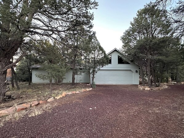 A residential property with a garage, surrounded by trees and a gravel driveway. - Upscale Mountain Retreat in Peaceful Pines! (Heber-Overgaard)