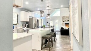 A modern kitchen with white cabinetry, a central island with stools, and a dining area with a black sofa. - Upscale Mountain Retreat in Peaceful Pines! (Heber-Overgaard)