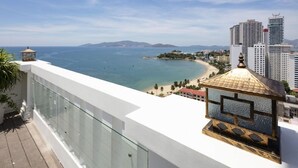 A balcony with a glass railing overlooking a beach and cityscape. - Aston Nha Trang City Hotel (Nha Trang)