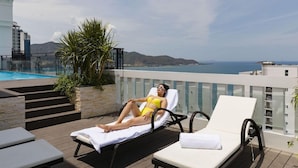 A poolside area with lounge chairs, a pool, and a view of the sea. - Aston Nha Trang City Hotel (Nha Trang)