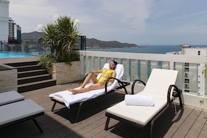 A poolside area with lounge chairs, a pool, and a view of the sea. - Aston Nha Trang City Hotel (Nha Trang)
