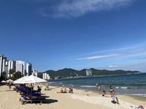 Uma praia com guarda-sóis, espreguiçadeiras e pessoas.