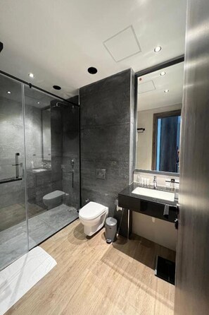 Un baño moderno con cabina de ducha de vidrio, inodoro, lavabo y espejo.