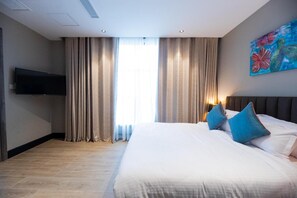 Una habitación de hotel con una cama grande, cortinas, un televisor de pantalla plana y un cuadro en la pared.