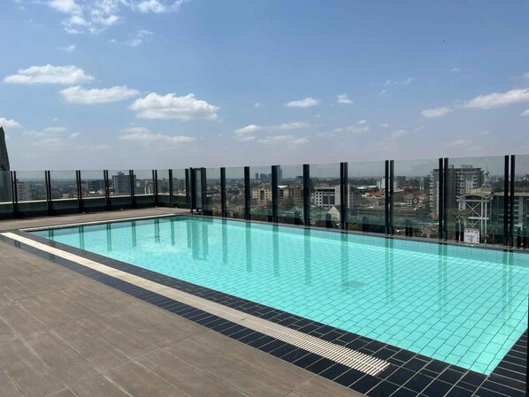 Una piscina en la azotea con vistas a la ciudad, rodeada de barandas de vidrio.