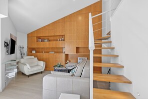 Ein modernes Wohnzimmer mit Treppe, einem weißen Sofa, einem Glastisch und Holzregalen.