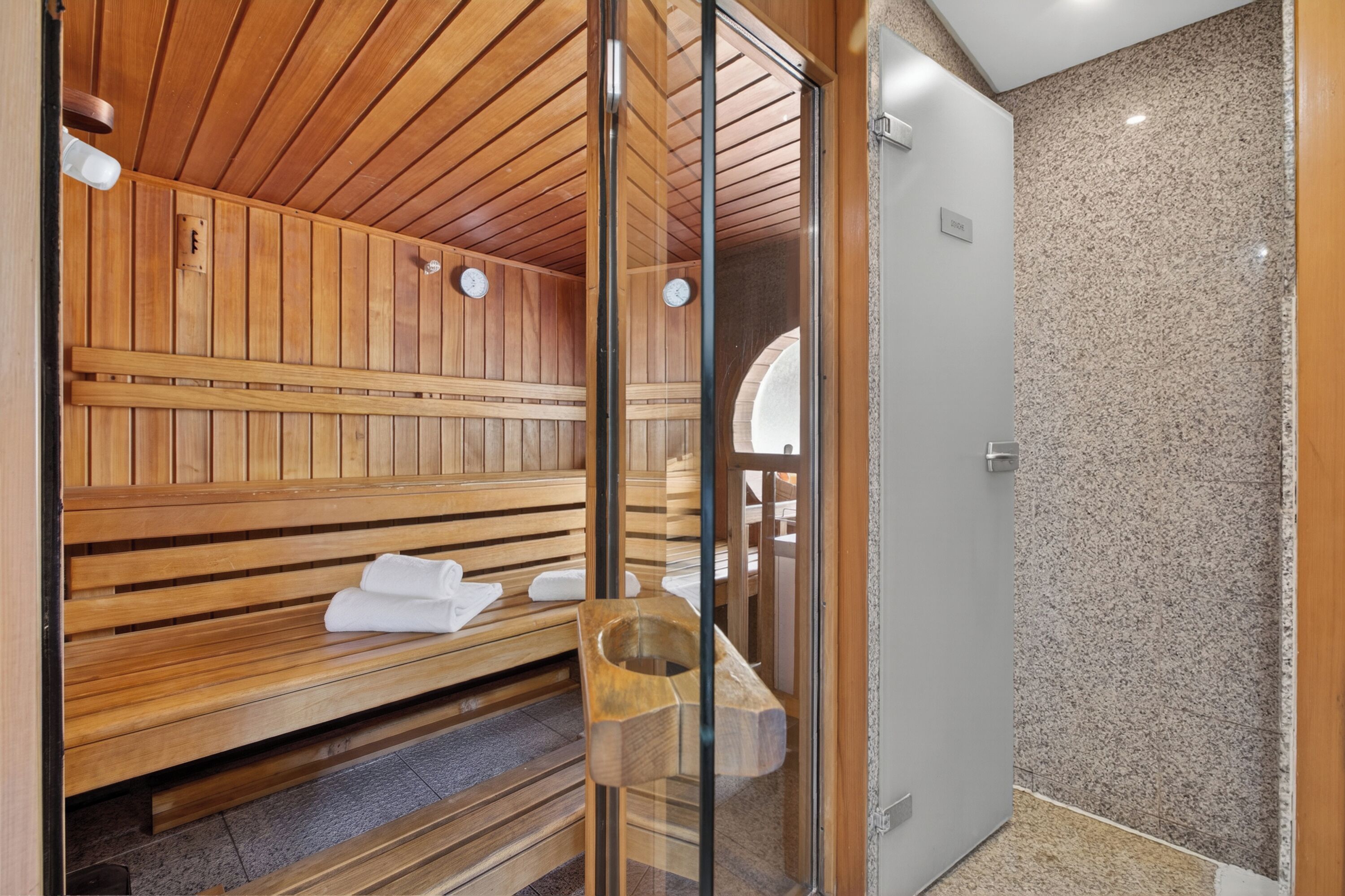 Ein Saunaraum mit Holzbänken und einer Glastür zum Duschbereich.