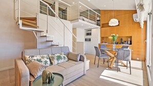 Ein zeitgemäßer Wohnraum mit einer Couch, einem Esstisch, Stühlen, einem Couchtisch, einer Treppe und einer Küchenzeile.