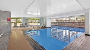 Ein Innenpool mit Holzterrasse, Liegestühlen und Blick auf ein Gebäude mit Balkon.