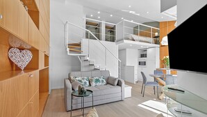 Ein modernes Wohnzimmer mit einer Couch, einem Glastisch, einem Fernseher und einer Treppe, die in eine obere Etage führt.
