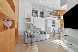 Ein modernes Wohnzimmer mit einer Couch, einem Glastisch, einem Fernseher und einer Treppe, die in eine obere Etage führt.
