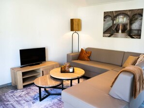Una sala de estar con televisor, sofá, mesa de centro, lámpara y obras de arte.