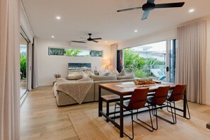 Un salon moderne comprenant un canapé, une table à manger avec des chaises, un ventilateur de plafond et une grande fenêtre donnant sur un paysage verdoyant.