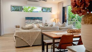 A modern living room with a sofa, a coffee table, and a dining area. - Trinity Beach Coastal Luxe Pool Retreat – 4BR (Trinity Beach)