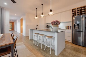Une cuisine moderne dotée d’un îlot central, de tabourets de bar, de luminaires suspendus et d’un réfrigérateur en acier inoxydable.