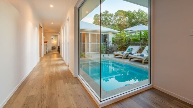 A modern interior with a glass wall leading to an outdoor pool area. - Trinity Beach Coastal Luxe Pool Retreat – 4BR (Trinity Beach)