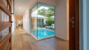 A modern interior with a glass wall leading to an outdoor pool area. - Trinity Beach Coastal Luxe Pool Retreat – 4BR (Trinity Beach)