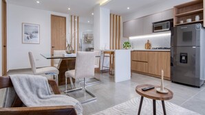 Une cuisine moderne équipée d’un réfrigérateur, d’un four à micro-ondes et de meubles de rangement en bois. On y trouve également un coin repas avec une table et des chaises en verre.