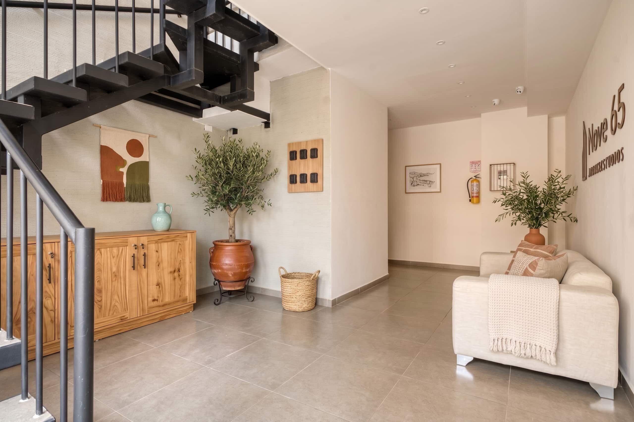 A modern interior with a staircase, a wooden cabinet, a white sofa, and two potted plants.