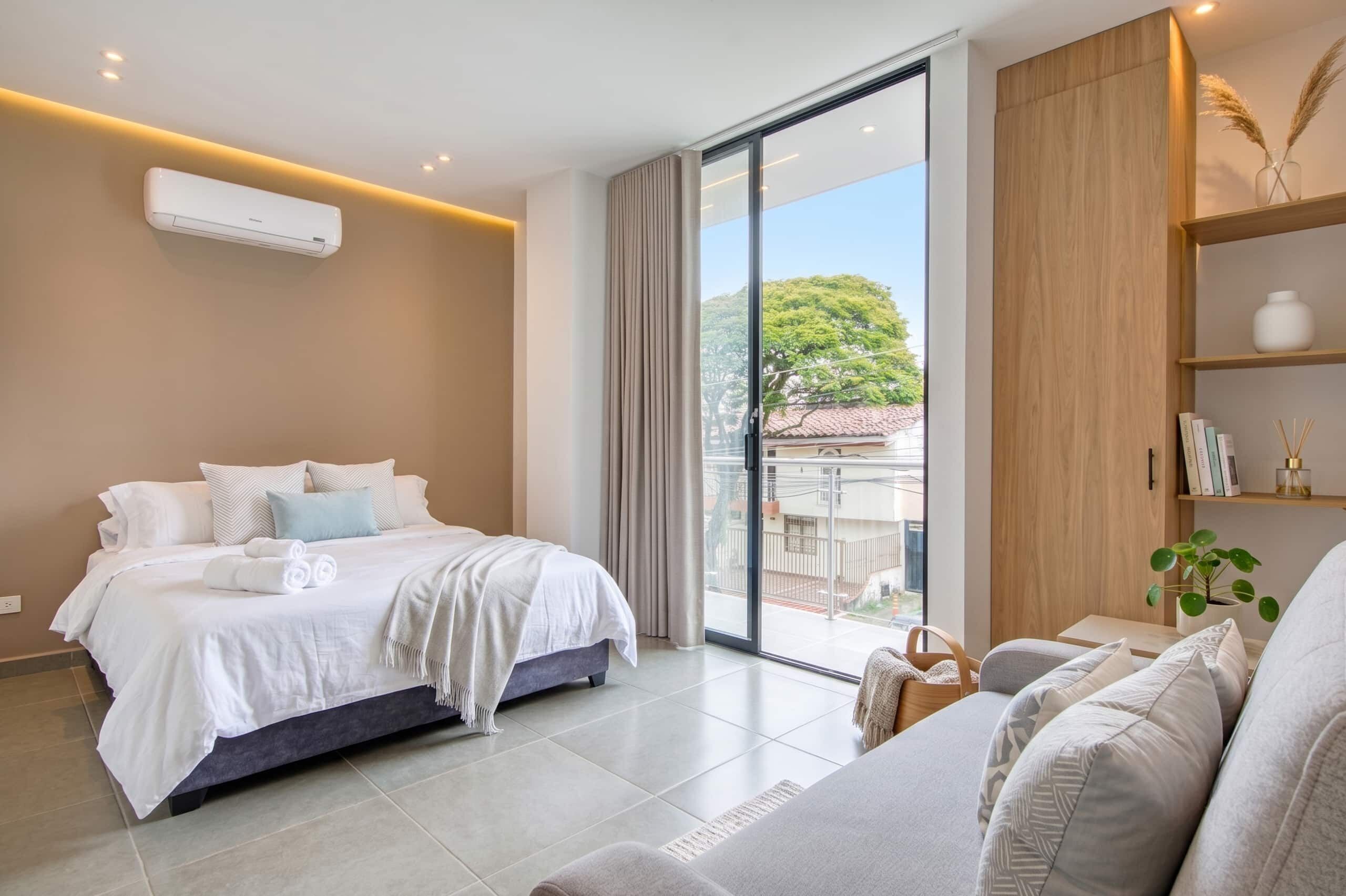 Un dormitorio moderno con cama, sofá, ventana grande y armario empotrado.