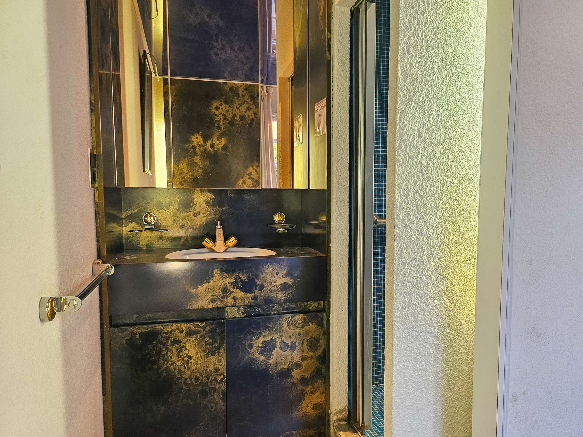Baño con lavamanos, espejo y puerta que da a otra habitación.