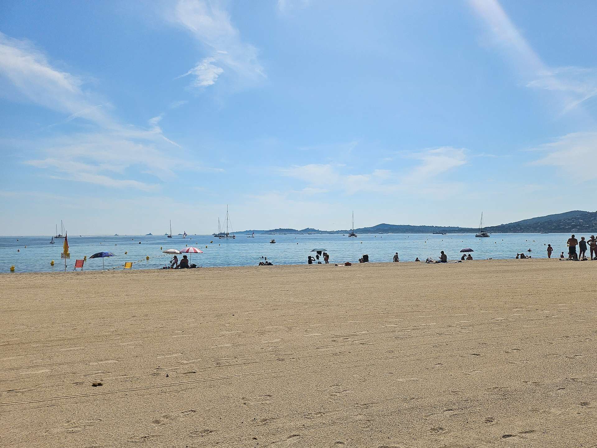 Una playa con arena, agua y barcos.