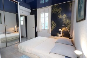 Ein Schlafzimmer mit einem Bett, einem Spiegel, einem Fenster mit Vorhängen und einer Statue.
