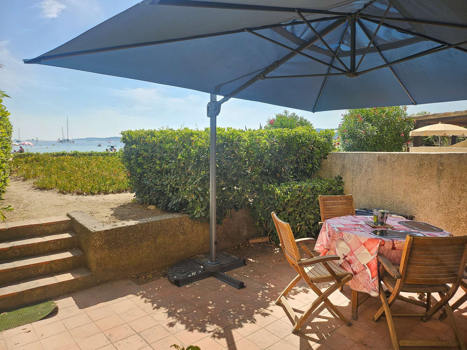 Un patio al aire libre con mesa y sillas, un paraguas grande y vistas al mar.